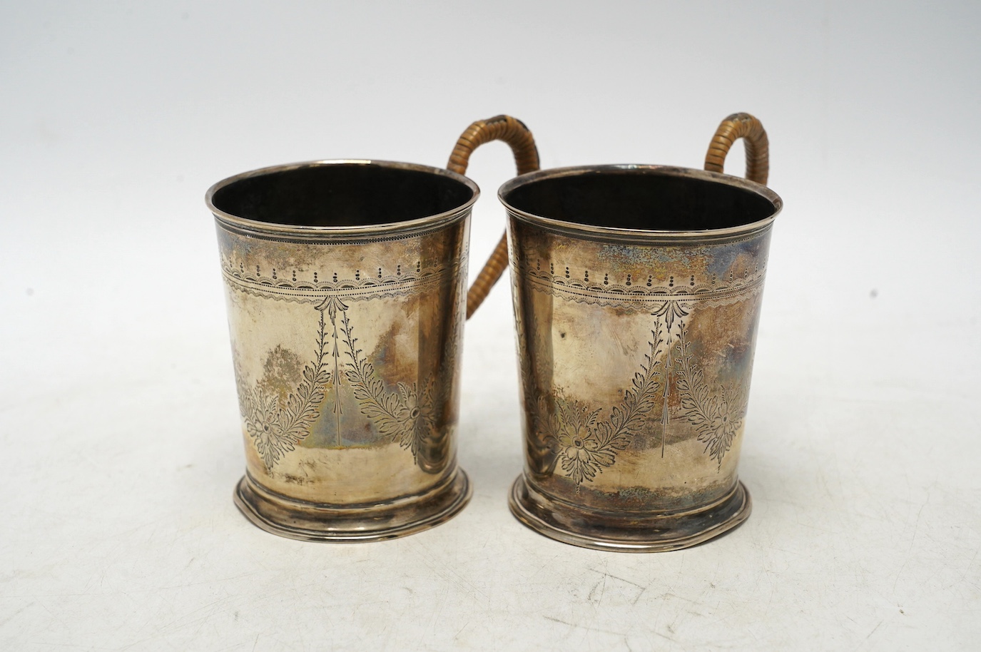 A pair of George V engraved silver mugs, with rattan handles, William Aitken, Birmingham, 1920, height 95mm, gross weight 5.9oz. Condition - fair